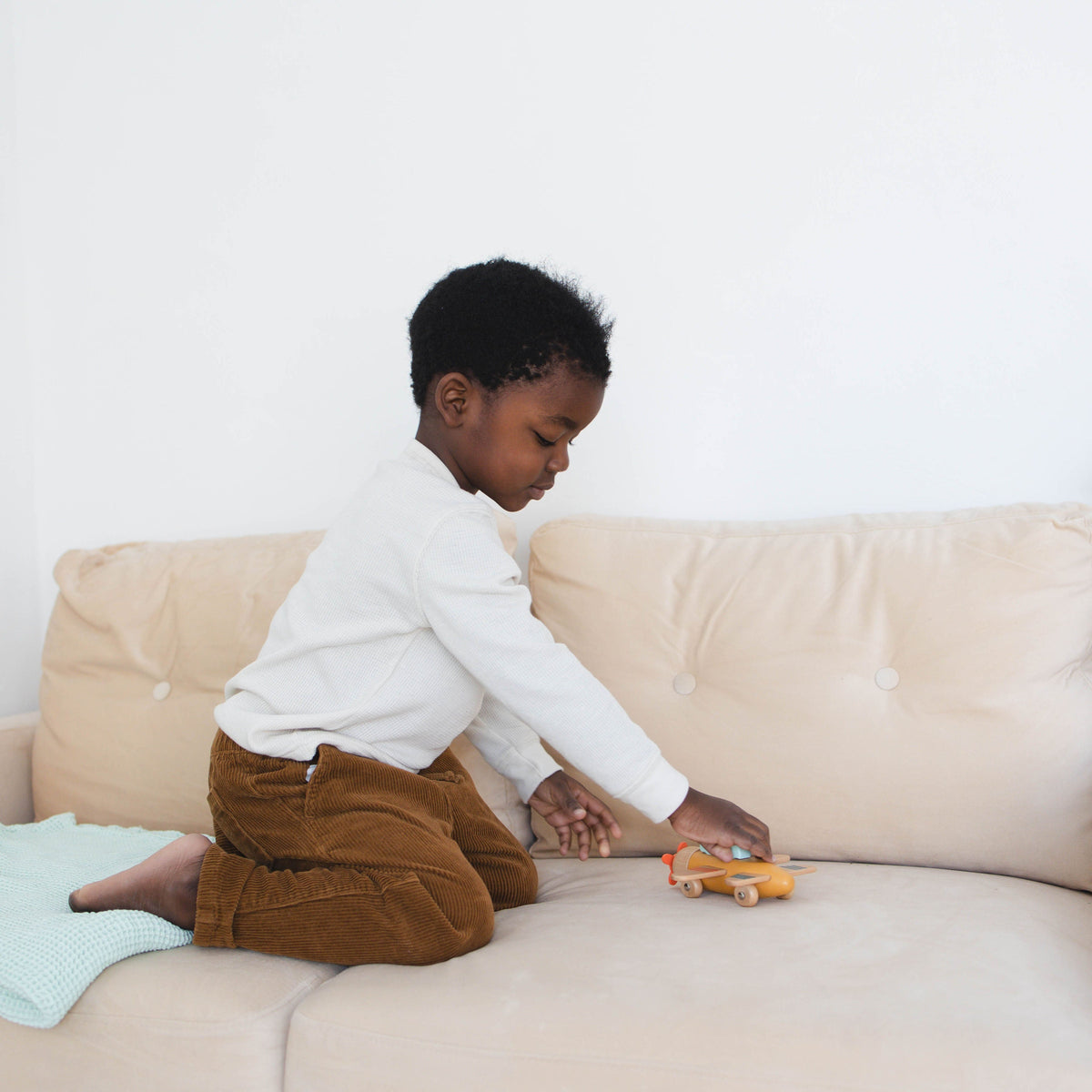 SpiritnSprout: Child rolling a wooden airplane along a sofa