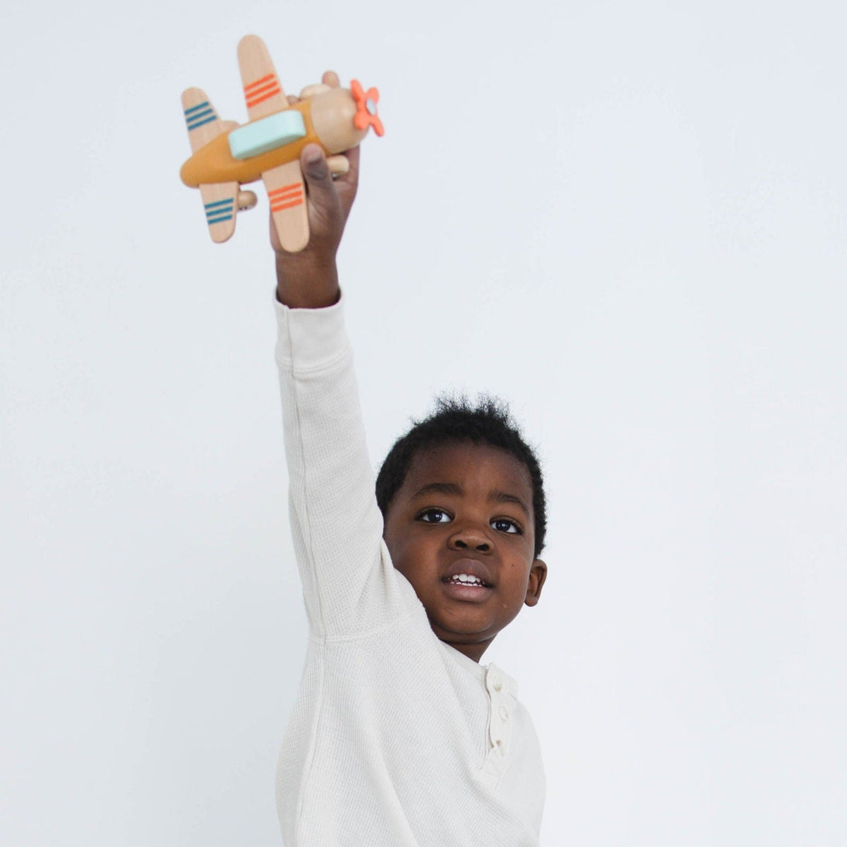 SpiritnSprout: Child holding a gold wooden airplane overhead