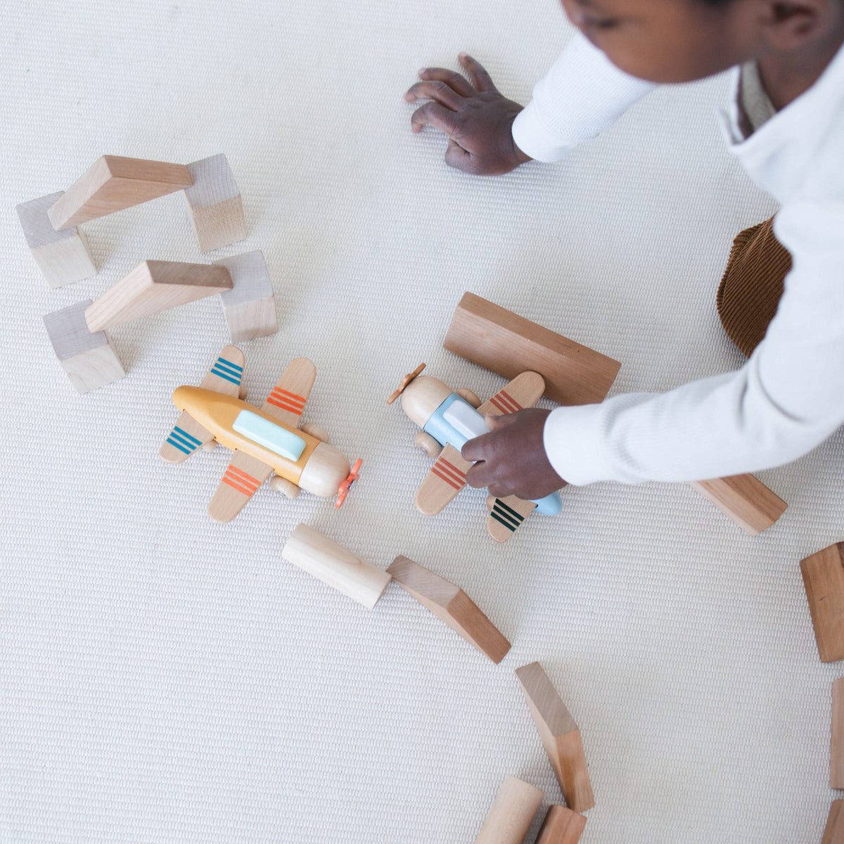 SpiritnSprout: Child playing with two wooden airplanes beside a block runway