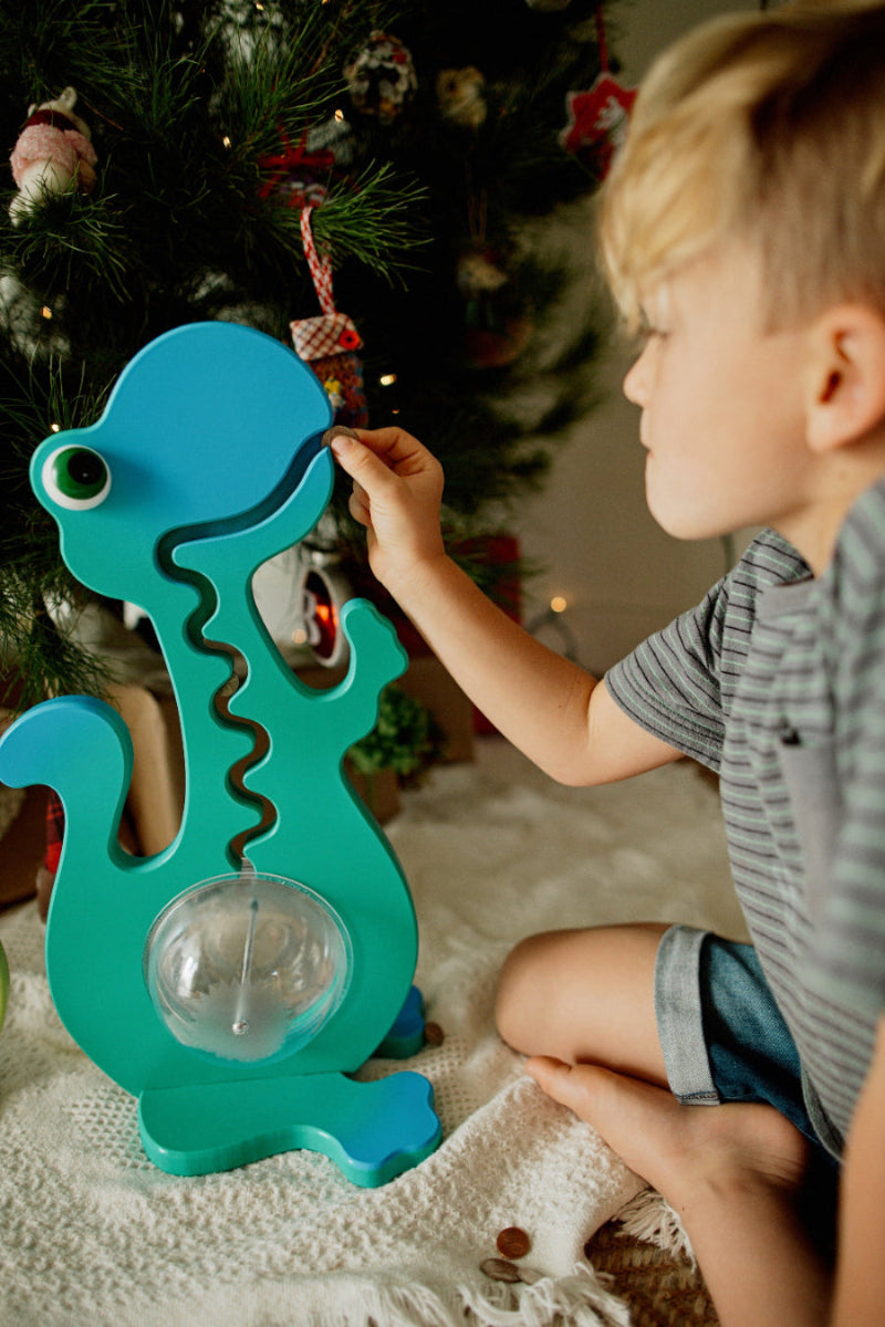 Child using an aqua dinosaur coin bank beside a decorated tree