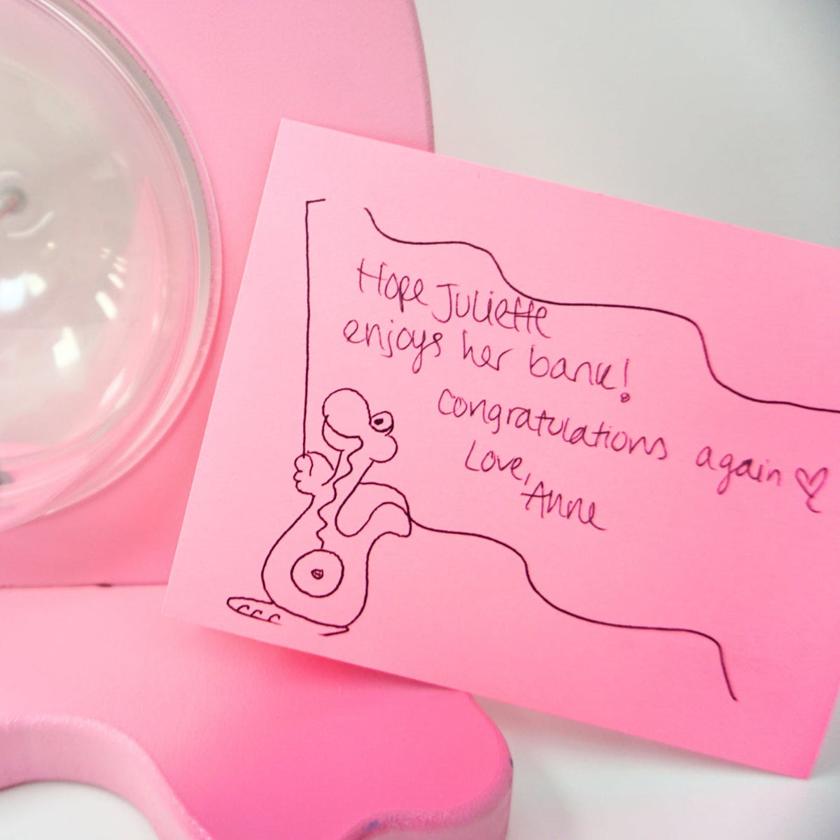 Handwritten gift note with a dinosaur drawing beside a pink dinosaur coin bank