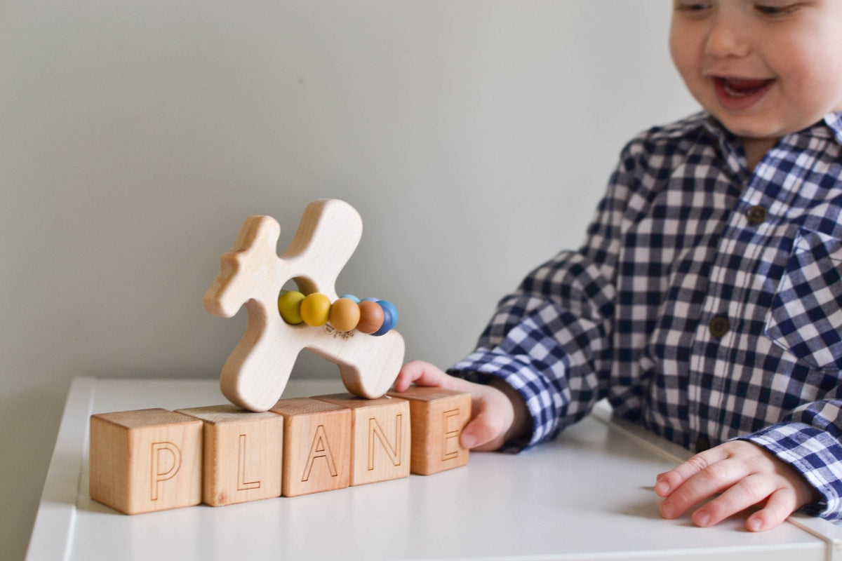 Child holding a wooden airplane grasping toy above letter blocks