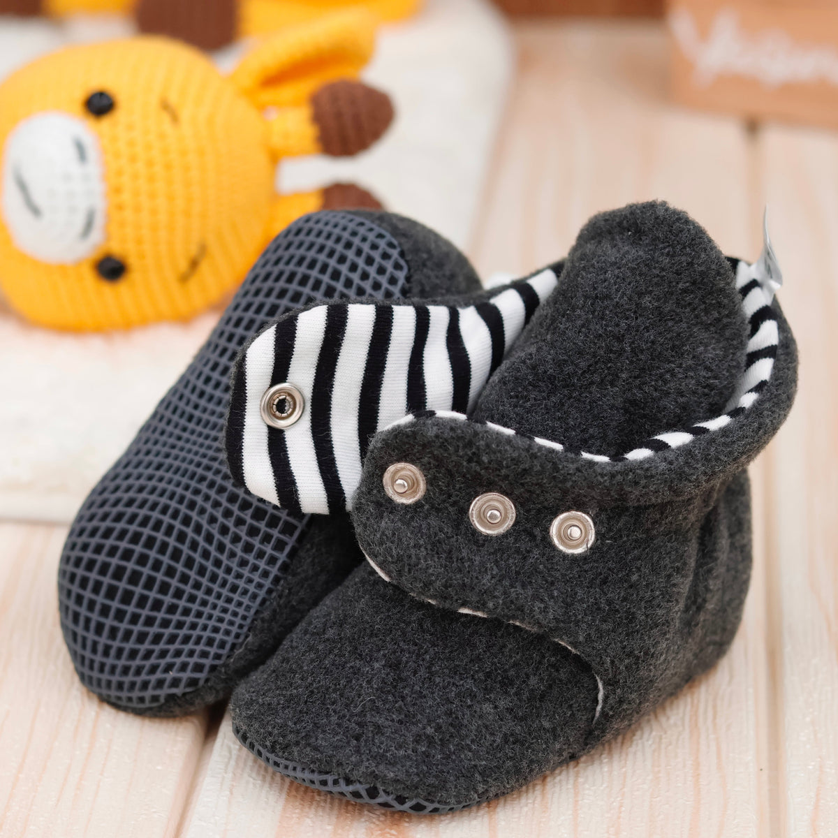 Close-up of charcoal fleece baby booties with striped lining and snap straps, showing one sole and an open snap strap.