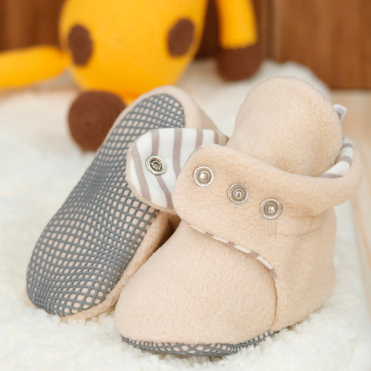 Close-up of cream fleece baby booties with pale striped lining and snap straps, showing one sole and an open snap strap.