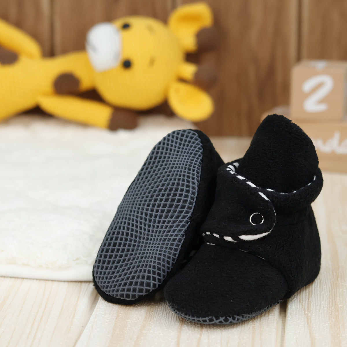 Black fleece baby booties with striped lining and snap straps arranged on a surface with one sole facing the camera.