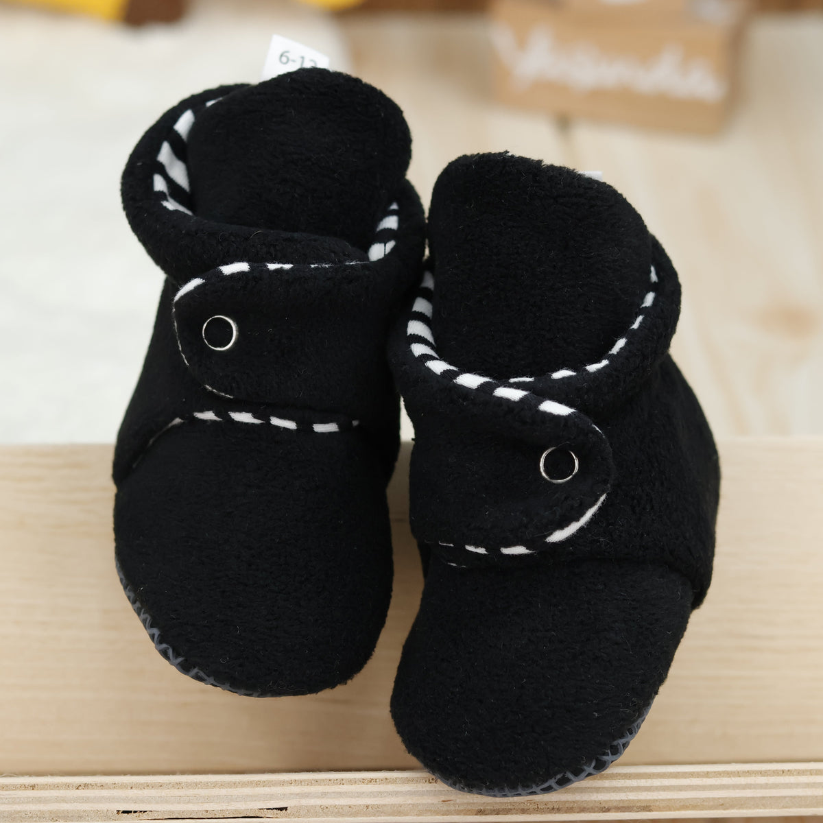 Front view of a pair of black fleece baby booties with striped lining and snap straps.