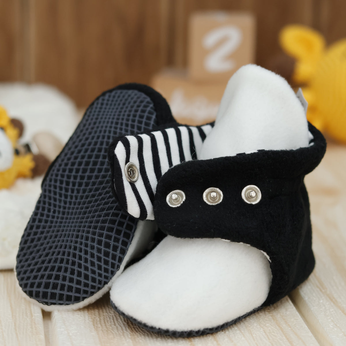 Close-up of black-and-white fleece baby booties with striped lining and snap straps, showing one sole and an open snap strap.