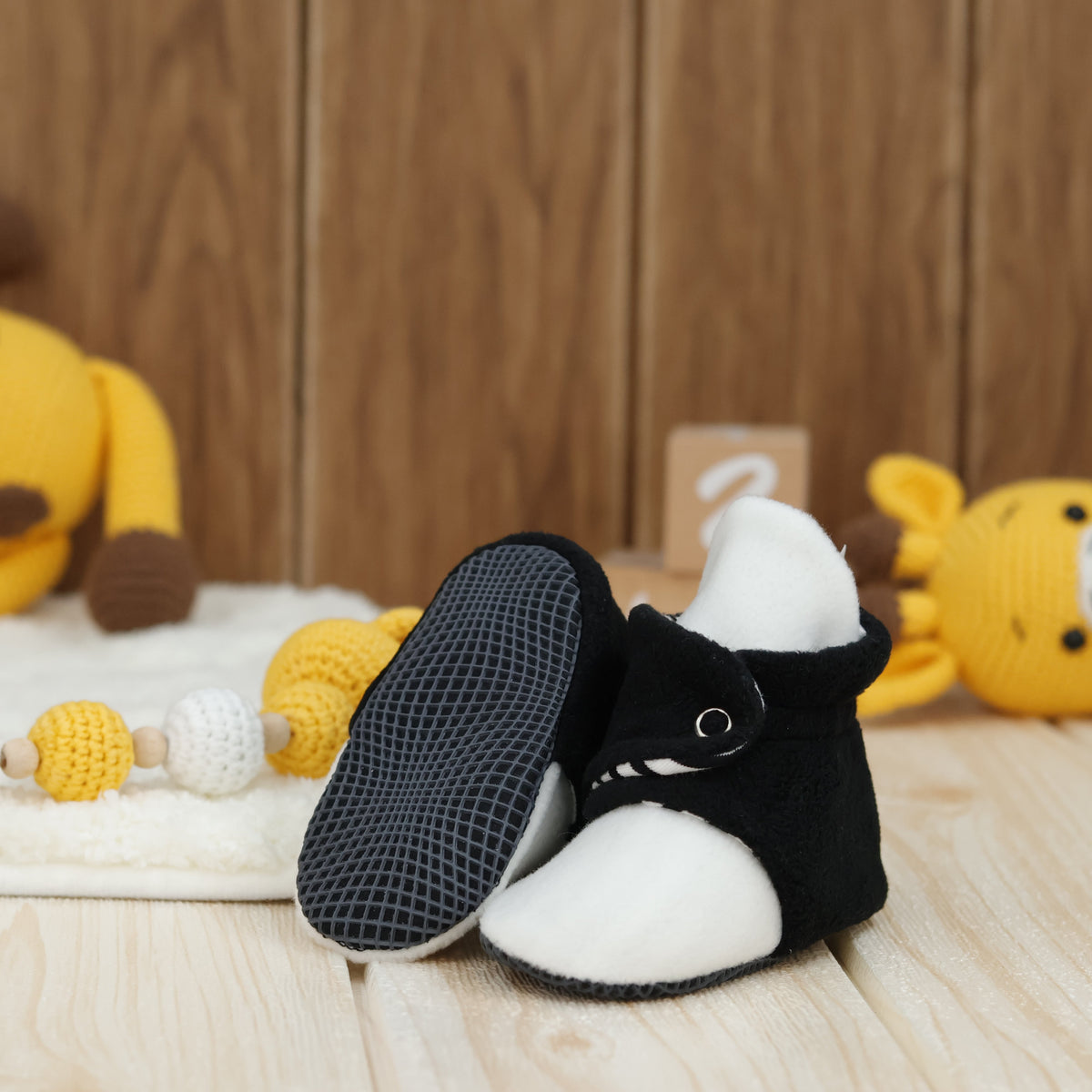Black-and-white fleece baby booties with striped lining and snap straps arranged on a surface with one sole facing the camera.
