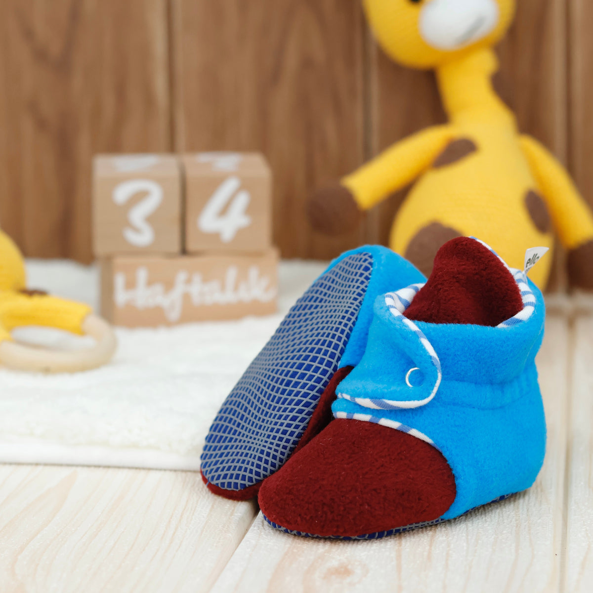 Blue-and-burgundy fleece baby booties with striped lining and snap straps arranged on a surface with one sole facing the camera.