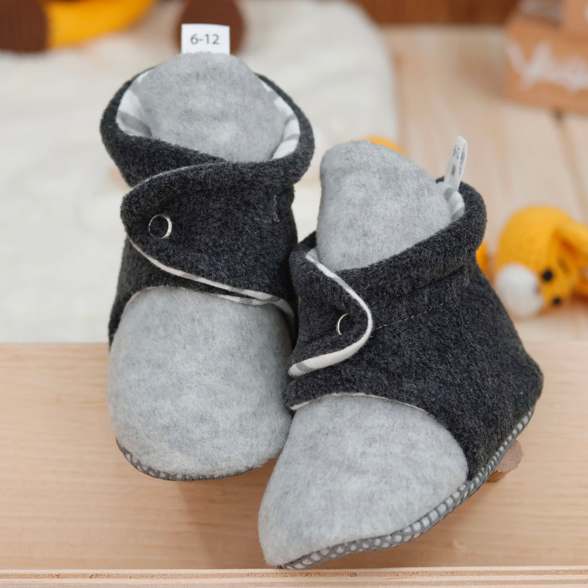 Front view of a pair of gray-and-charcoal fleece baby booties with striped lining and snap straps.