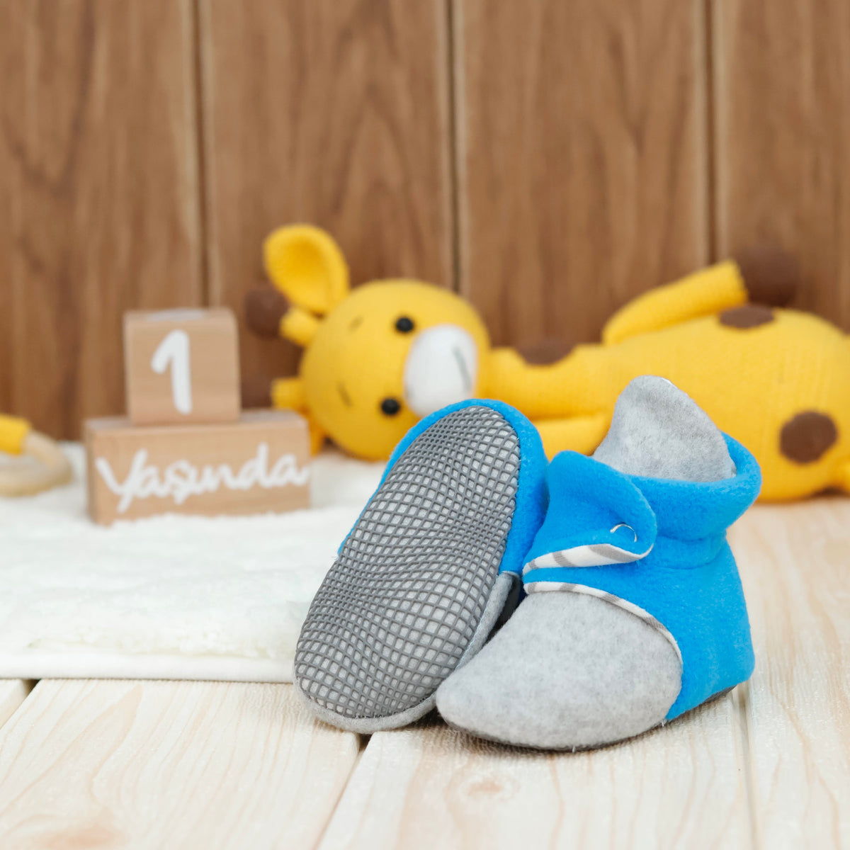 Blue-and-gray fleece baby booties with striped lining and snap straps arranged on a surface with one sole facing the camera.