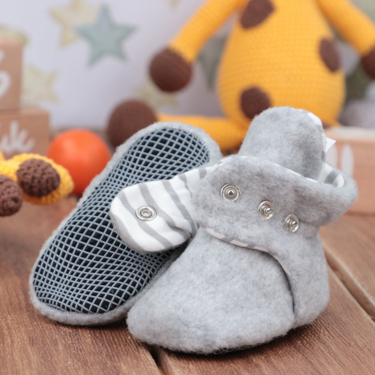 Close-up of light gray fleece baby booties with snap straps, showing one sole and an open snap strap.