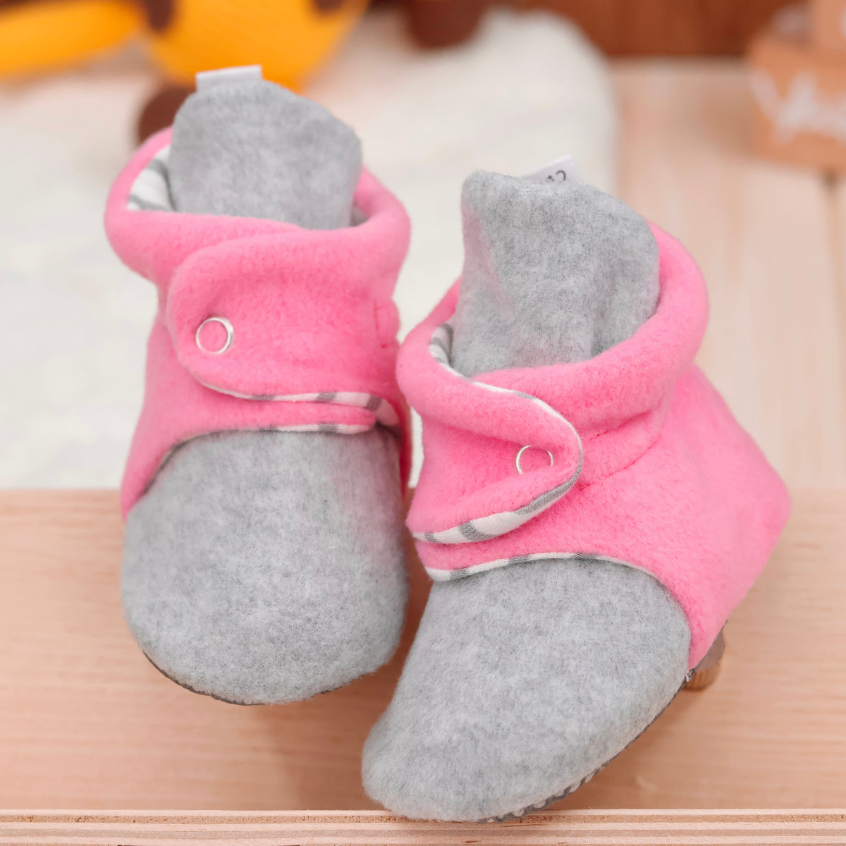 Front view of a pair of pink-and-gray fleece baby booties with striped lining and snap straps.