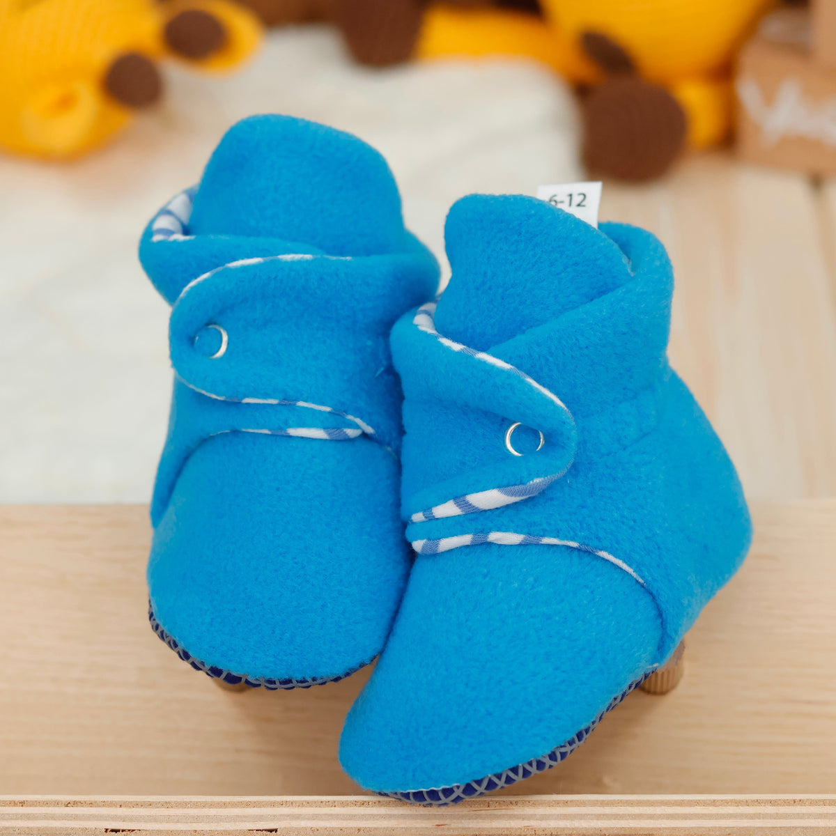 Front view of a pair of bright blue fleece baby booties with striped lining and snap straps.