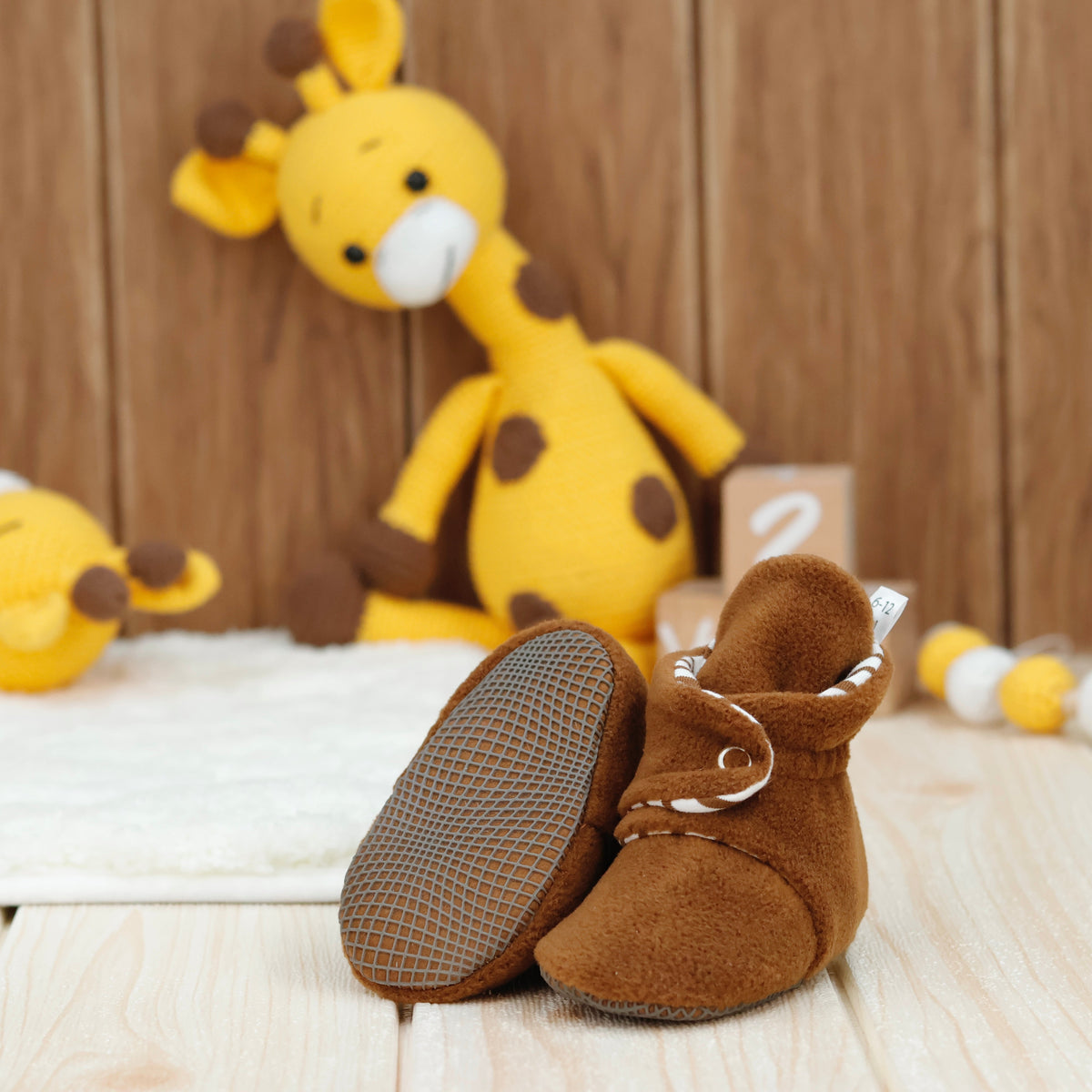 Warm brown fleece baby booties with striped lining and snap straps arranged on a surface with one sole facing the camera.