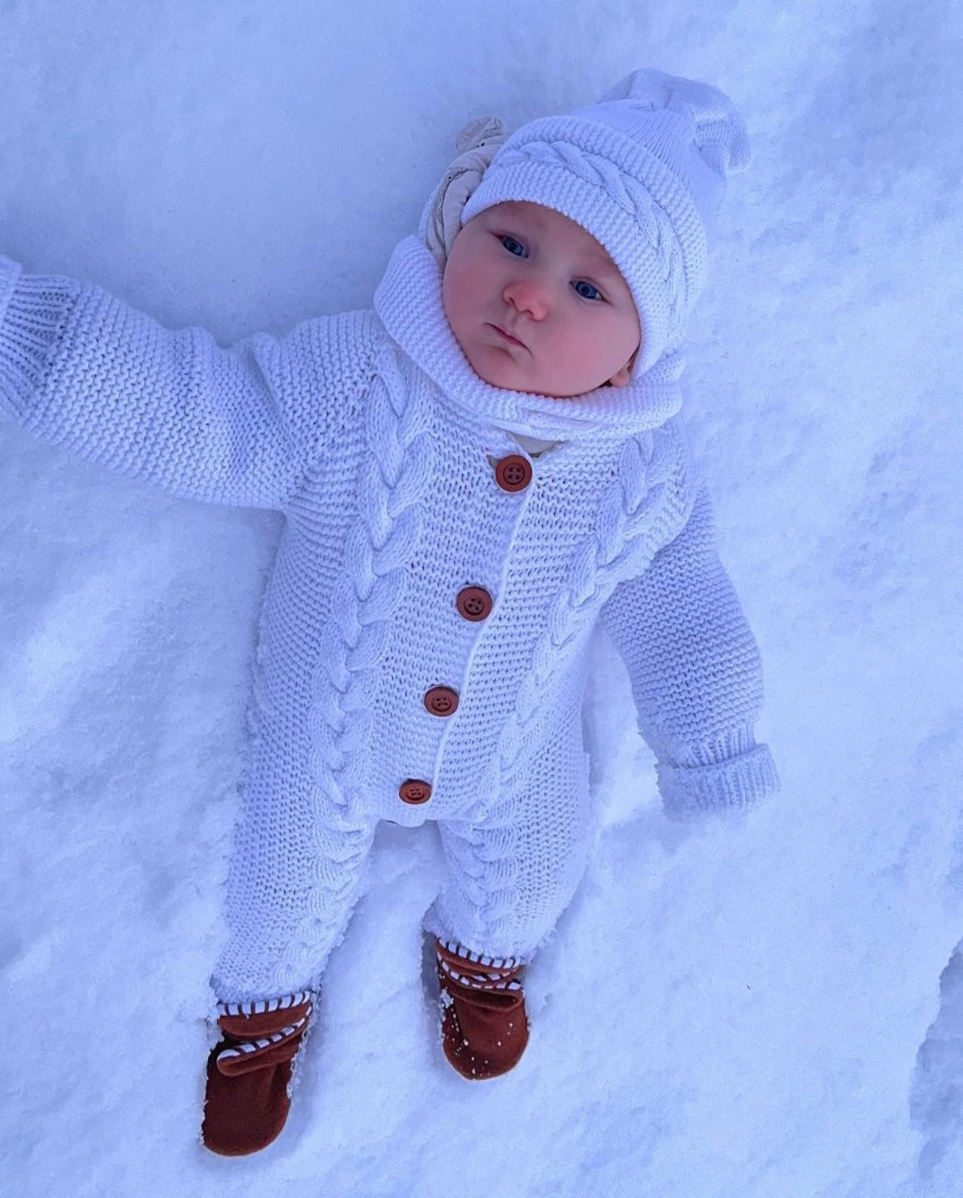 Closer view of a baby in a white outfit lying in snow wearing brown booties.