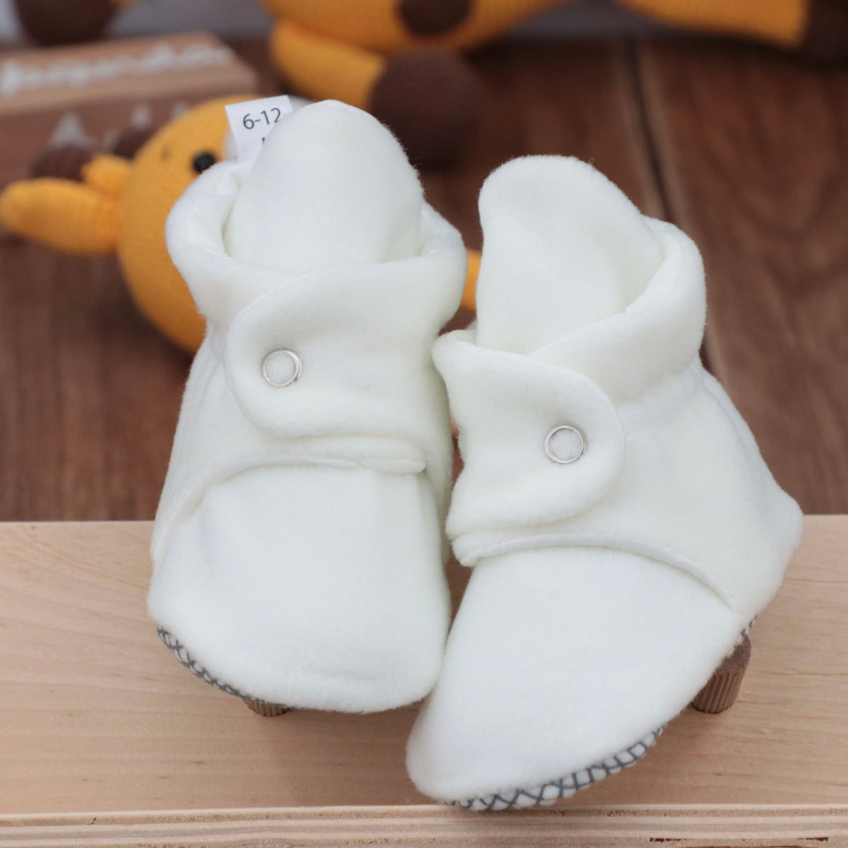 Front view of a pair of white fleece baby booties with snap straps.