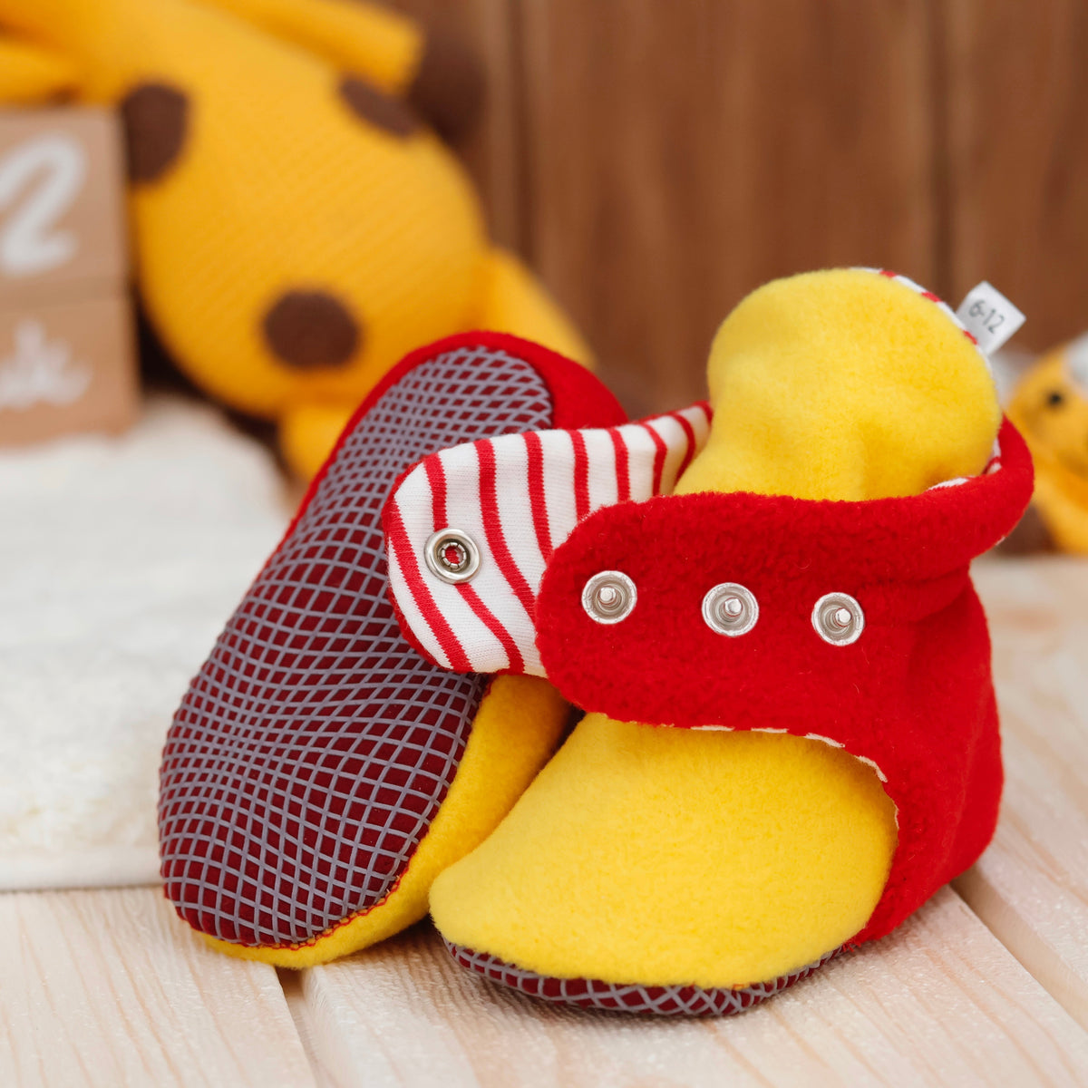 Close-up of red-and-yellow fleece baby booties with striped lining and snap straps, showing one sole and an open snap strap.