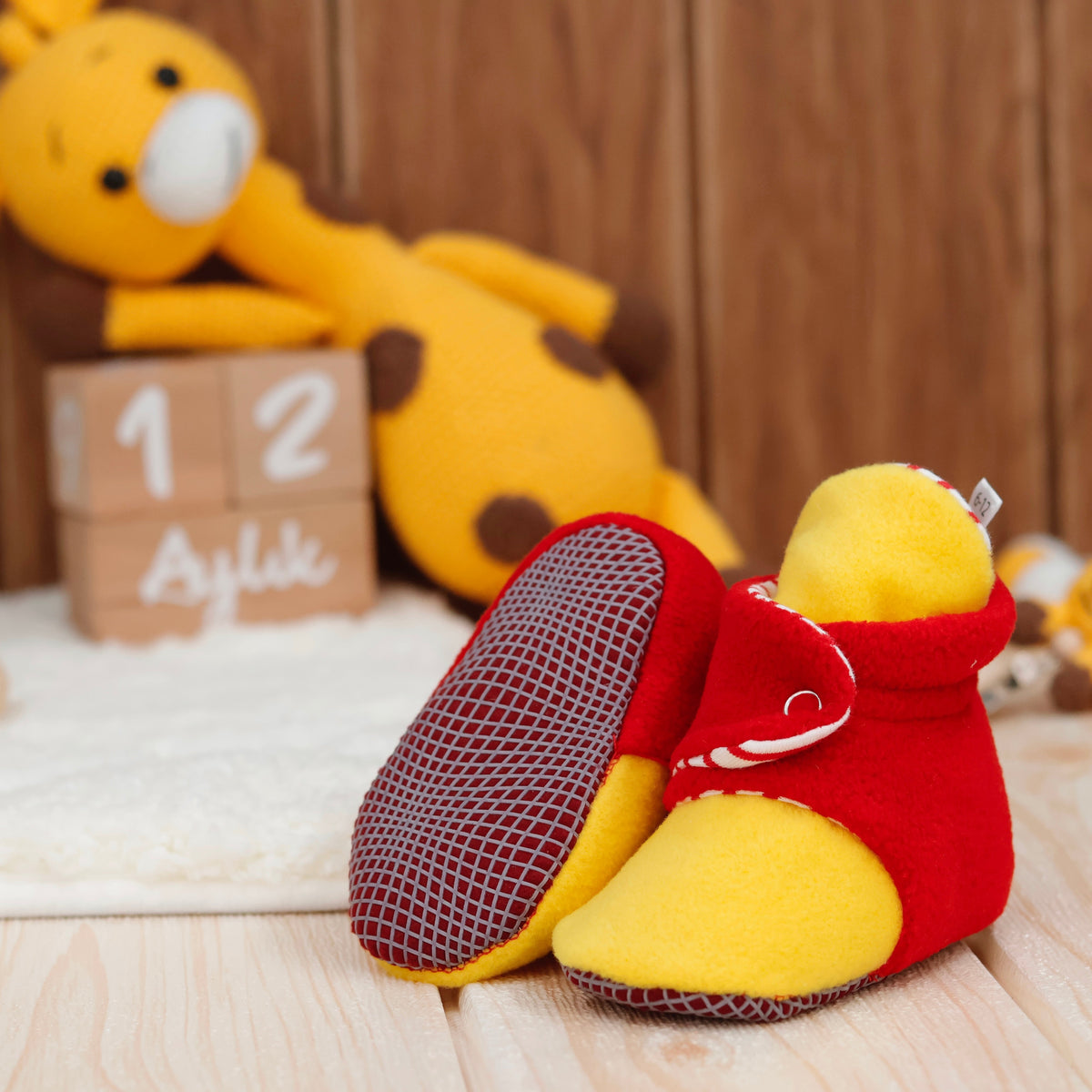 Red-and-yellow fleece baby booties with striped lining and snap straps arranged on a surface with one sole facing the camera.