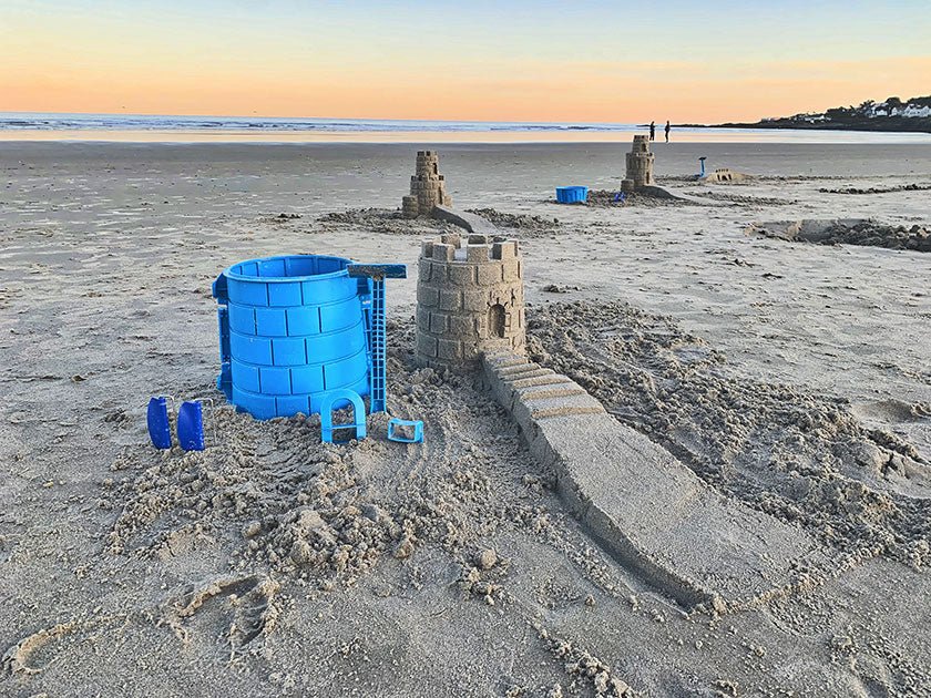 Blue Basic Tower mold and tools beside a sandcastle with a long staircase on a wide beach at sunset.