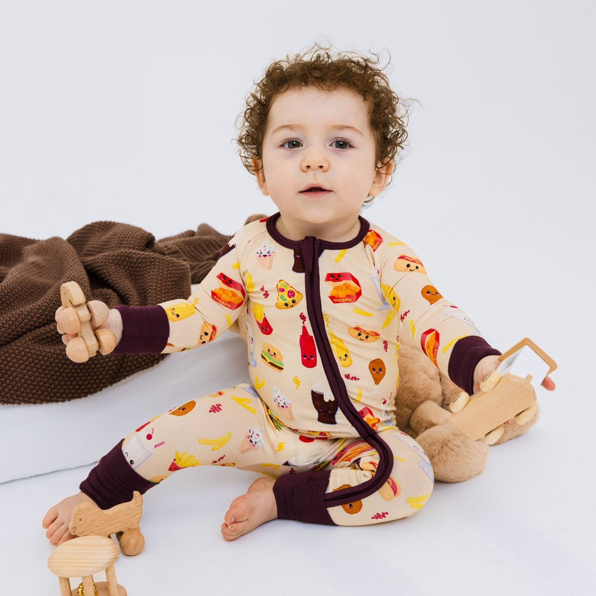 Baby seated with a wooden toy and soft toys while wearing Bam & Stitch Blissful Bites Convertible Romper.