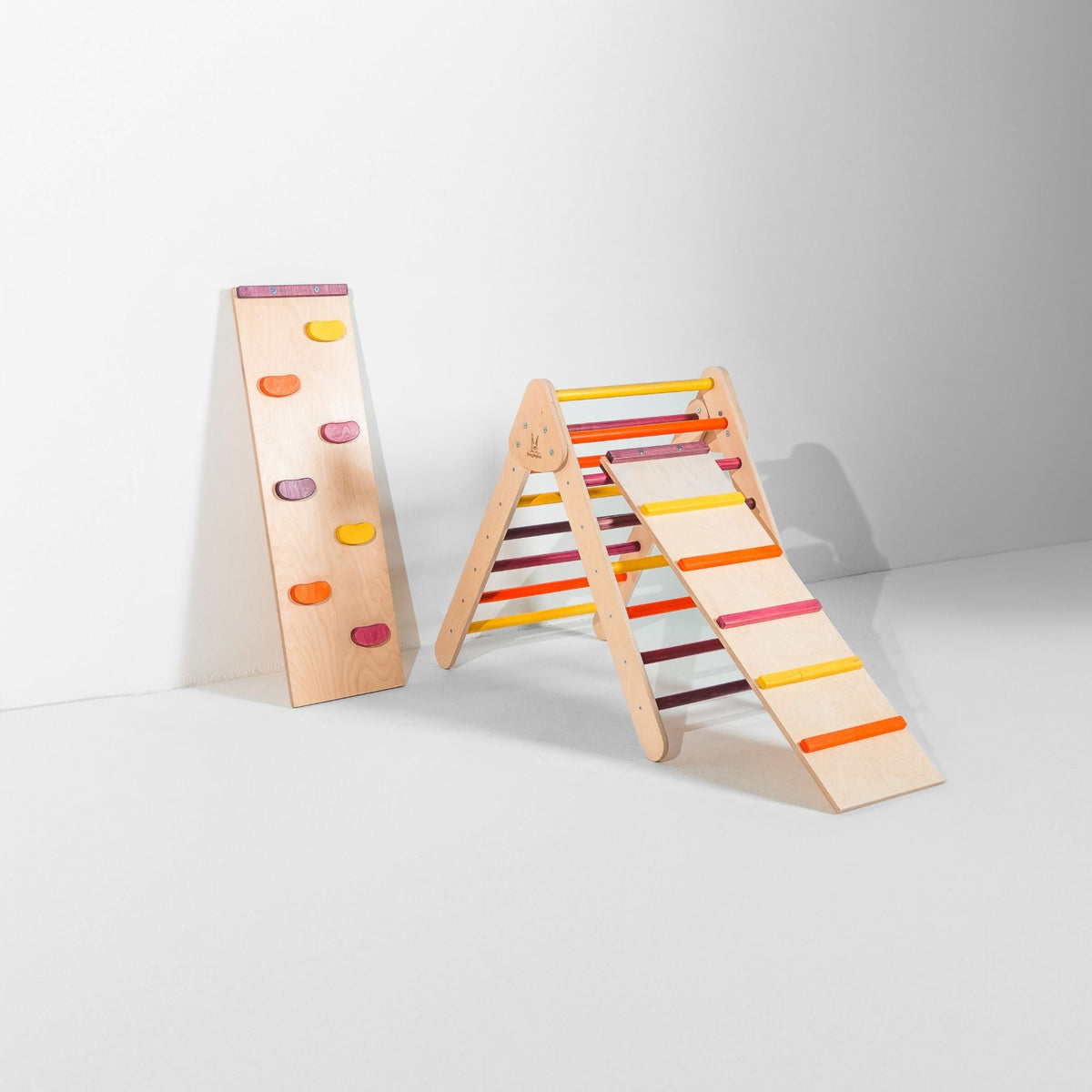 Pink, purple, orange and yellow triangle with attached ladder ramp and a climbing-hold ramp beside it.