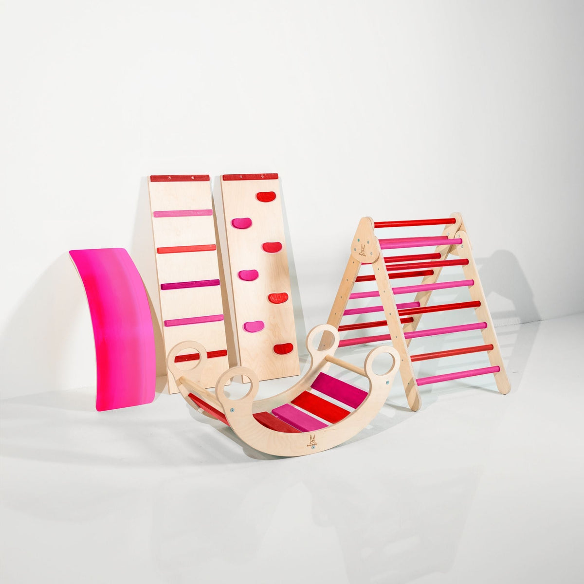 Red and pink climbing triangle, two ramps, curved wobble board and rocker displayed together.
