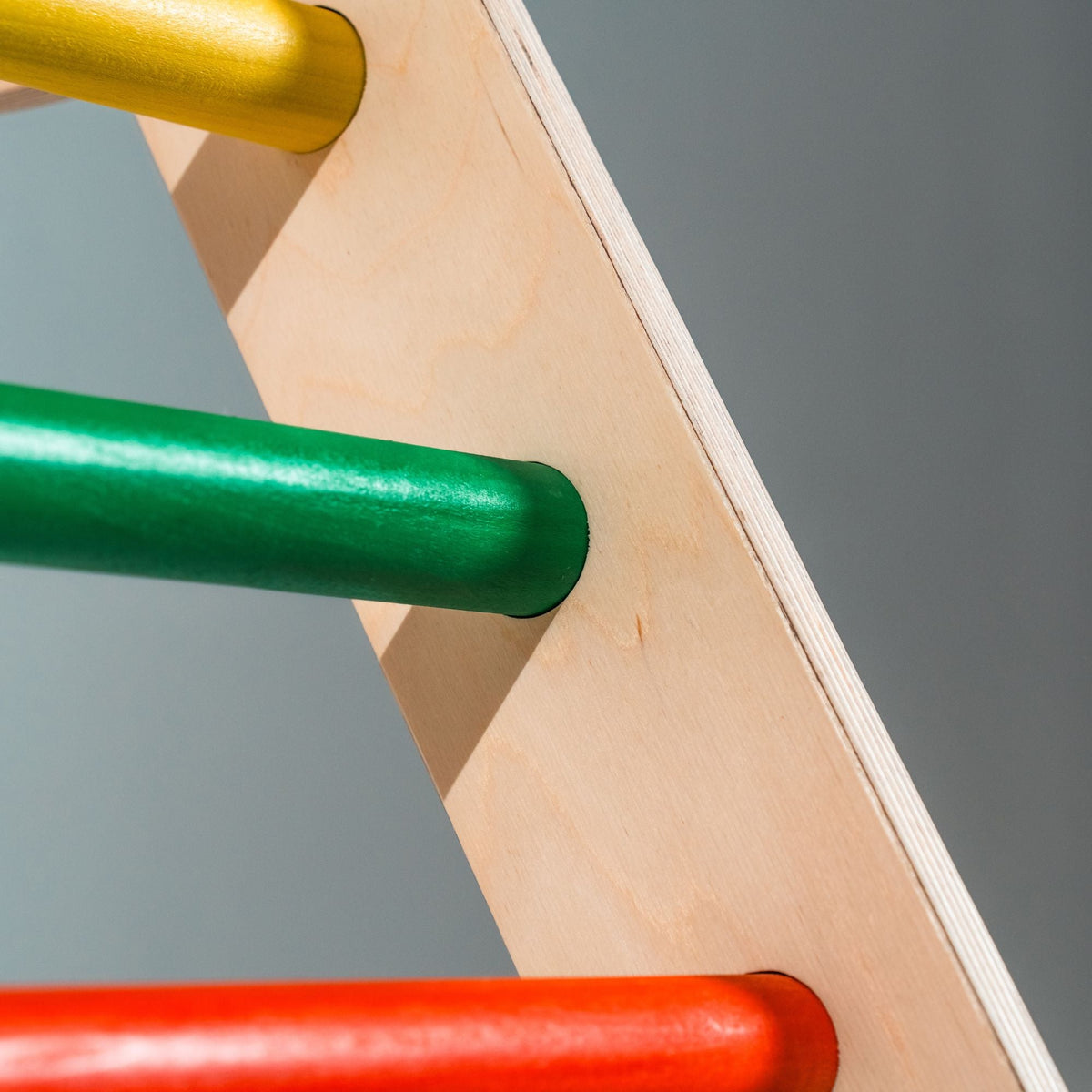 Close-up of green, yellow and red climbing-triangle rungs meeting a natural-tone side rail.
