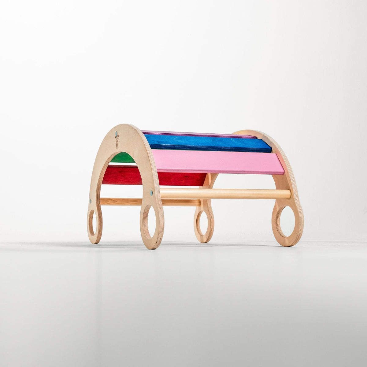 Rainbow-slat rocker turned upside down as an arch on a white floor.