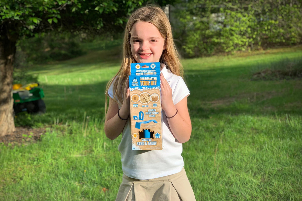 Person holding the boxed Create A Castle Build Master Tool Kit outdoors on grass.