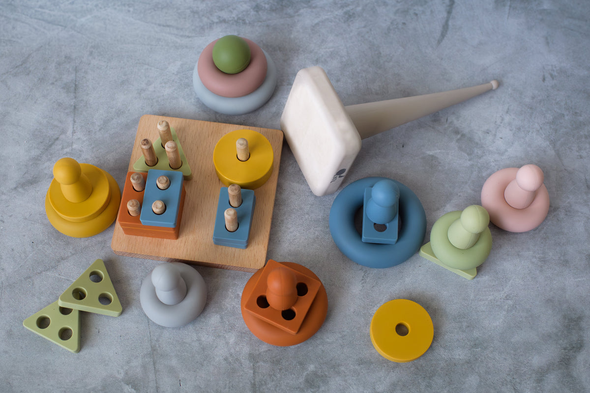 Overhead view of ring stacker parts, peg dolls, and shape puzzle pieces on a gray surface.