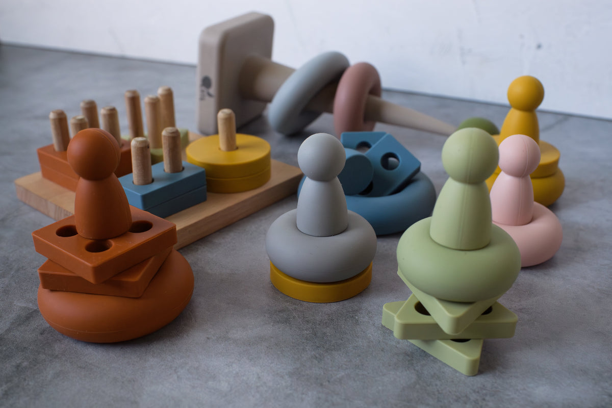 Close-up of peg dolls stacked with silicone rings and geometric puzzle pieces.