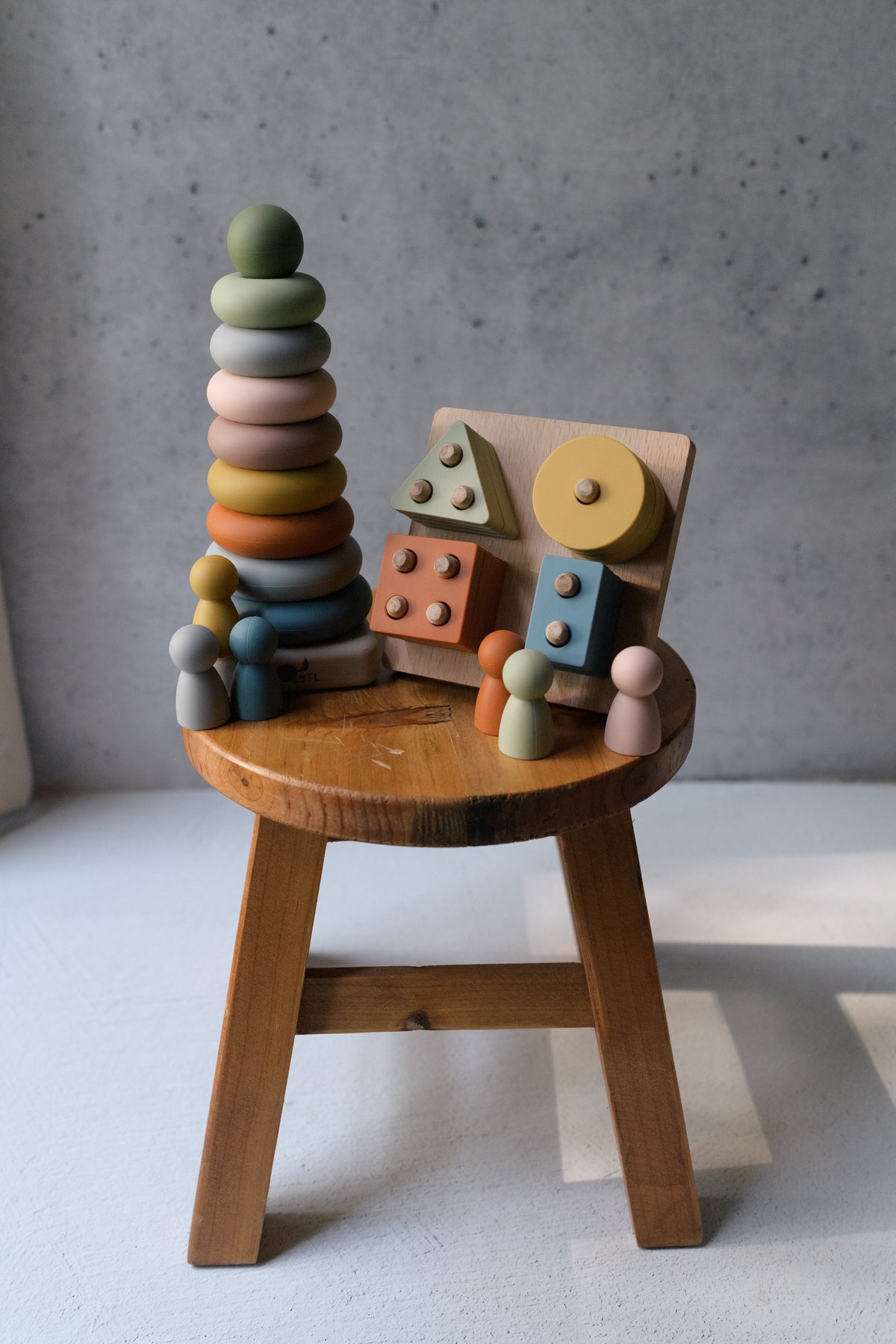 Ring stacker, shape puzzle, and silicone peg dolls displayed together on a wooden stool.