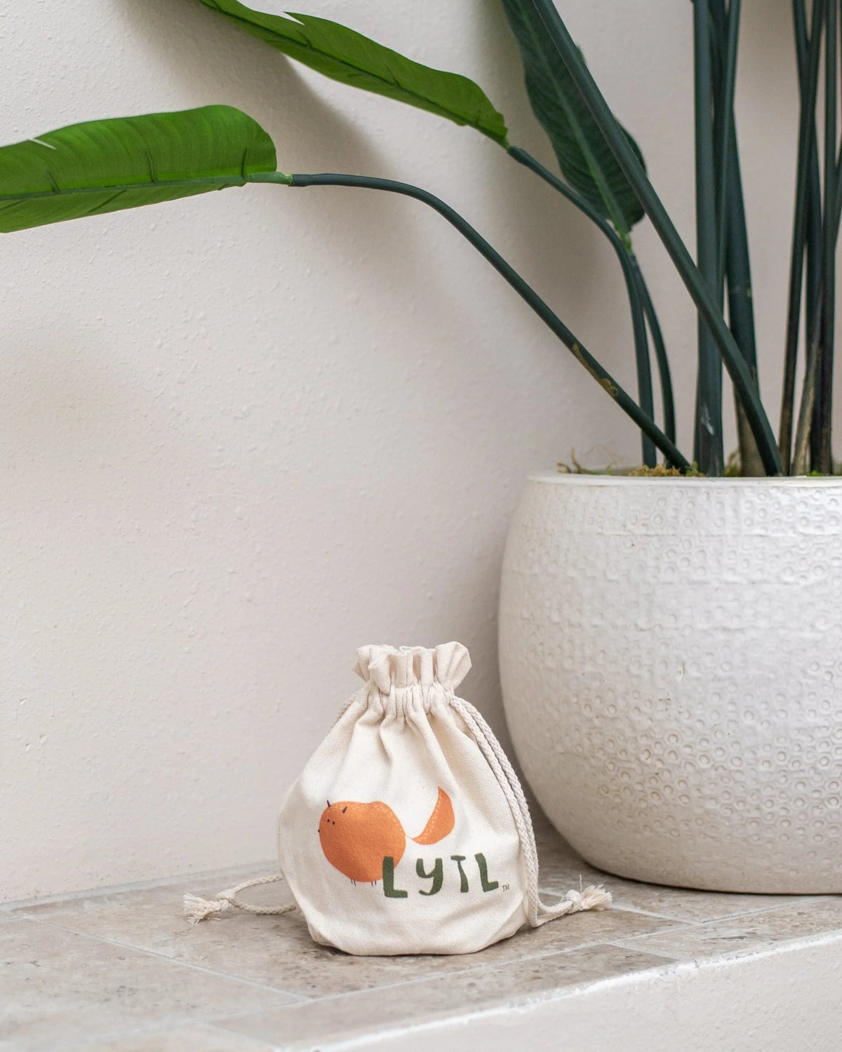 Small LYTL canvas drawstring bag beside a large white plant pot.
