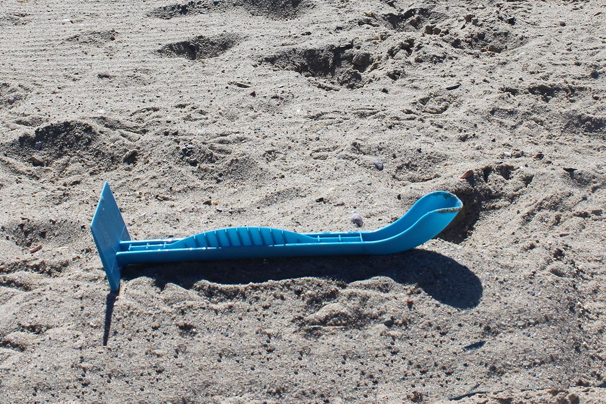 Blue two-ended sand-sculpting tool lying horizontally on beach sand.