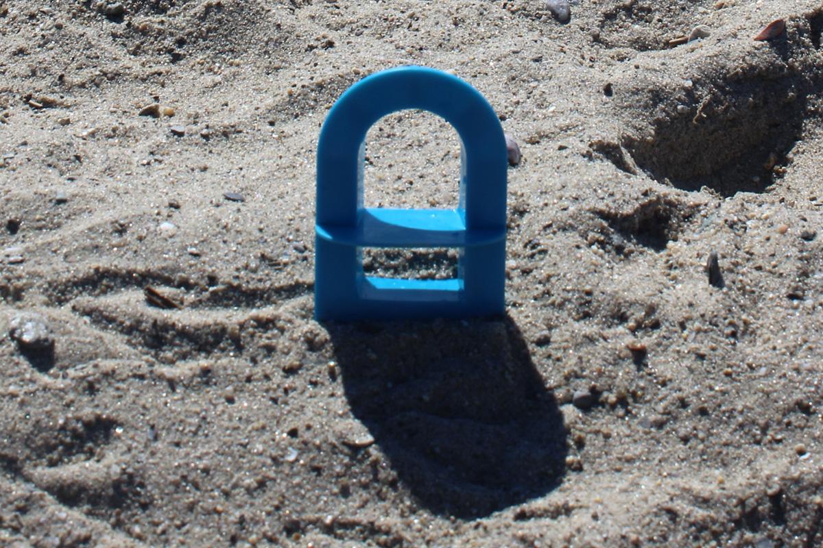 Blue arched window cutter viewed from the front, casting a shadow across beach sand.