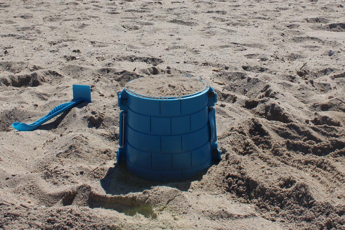 Large blue brick-pattern tower mold packed with sand, with a blue sculpting tool nearby.