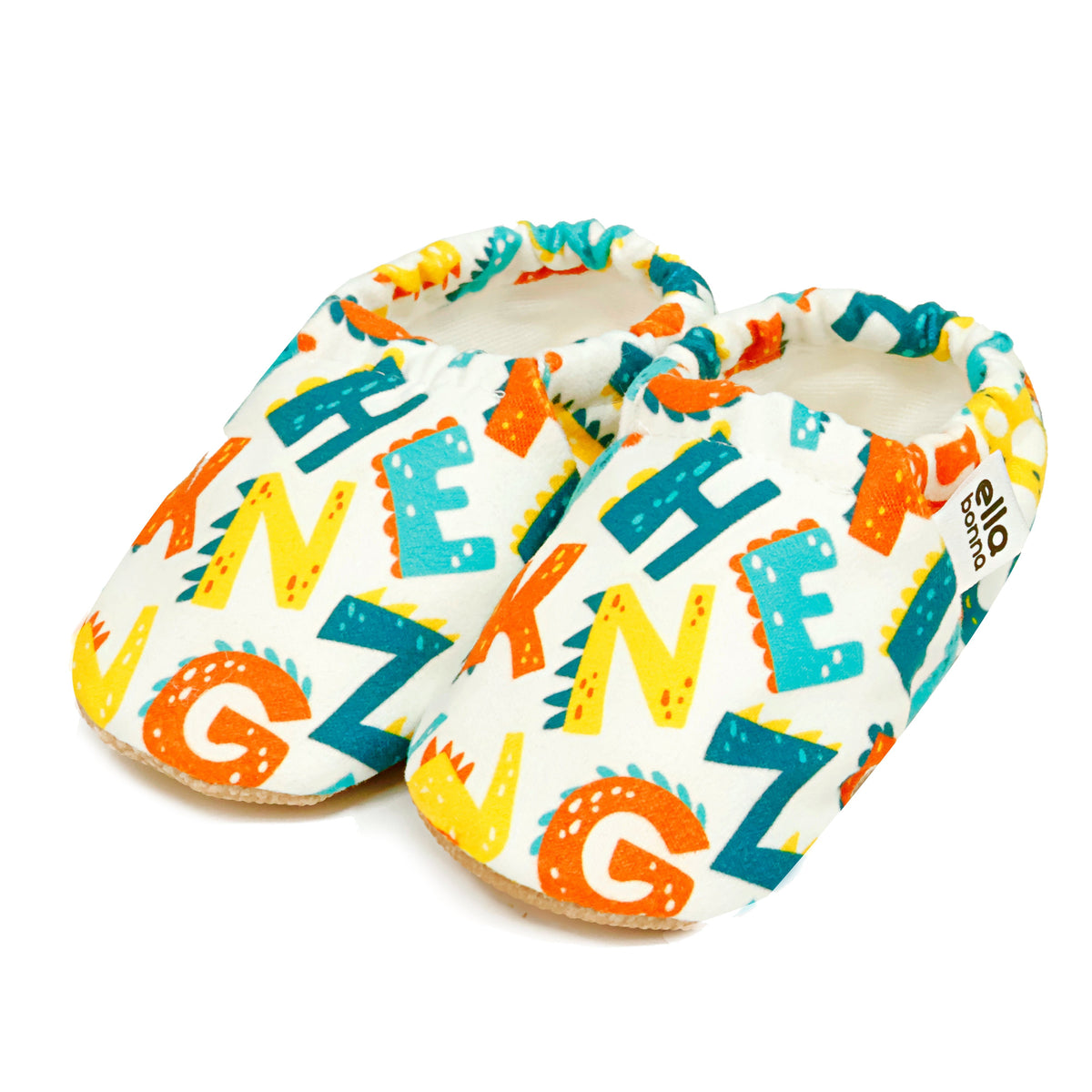 Pair of white slip-on baby moccasins with colorful alphabet print on a white background.