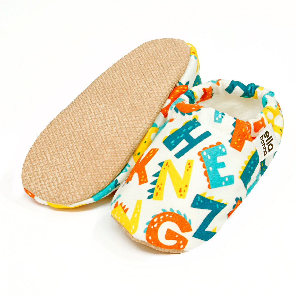 White slip-on baby moccasins with colorful alphabet print, with one sole facing the camera on a white background.