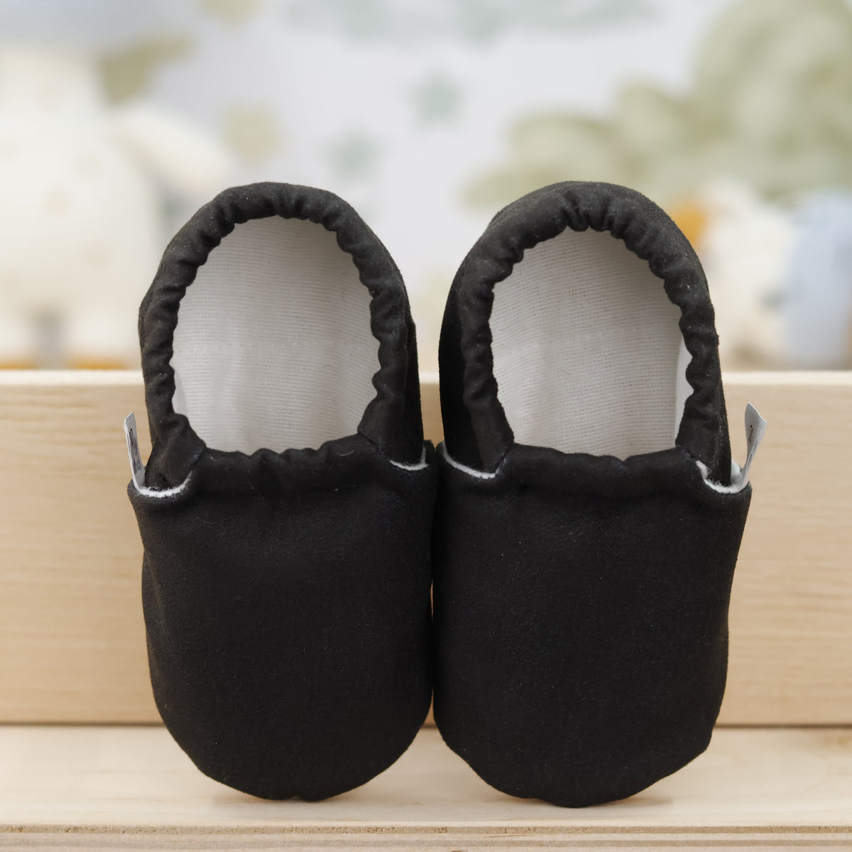 Front view of a pair of black slip-on baby moccasins with cream lining and tan soles.
