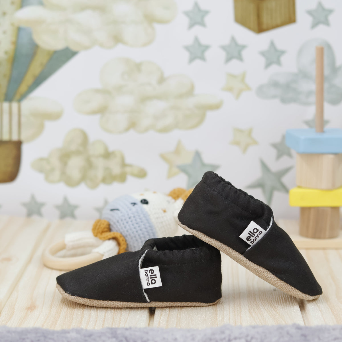 Black slip-on baby moccasins with cream lining and tan soles arranged together to show the sides and uppers.