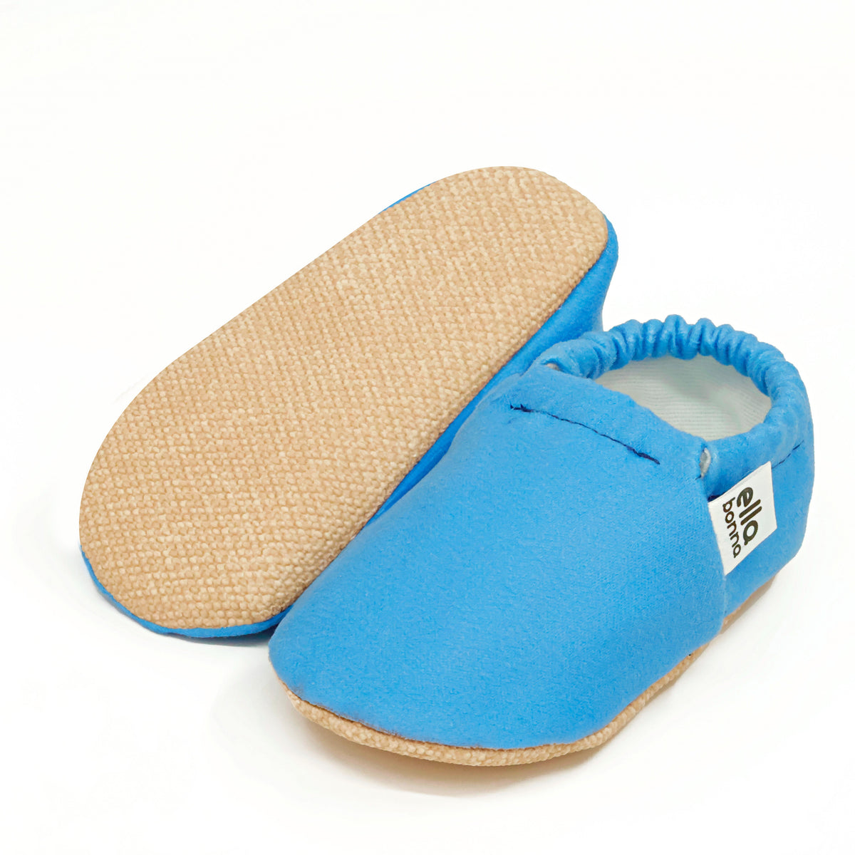 Blue slip-on baby moccasins with cream lining and tan soles, with one sole facing the camera on a white background.
