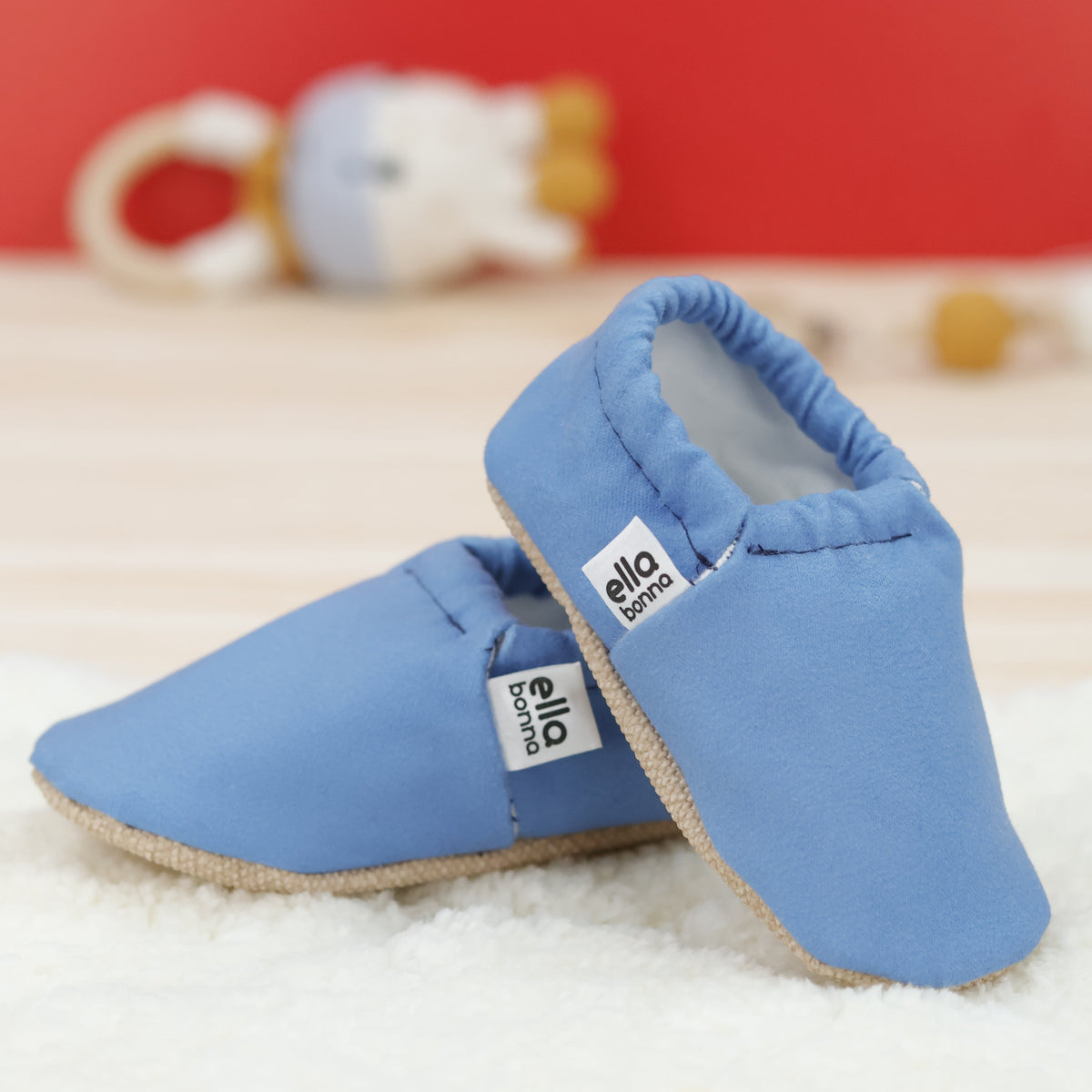 Blue slip-on baby moccasins with cream lining and tan soles arranged together to show the sides and uppers.