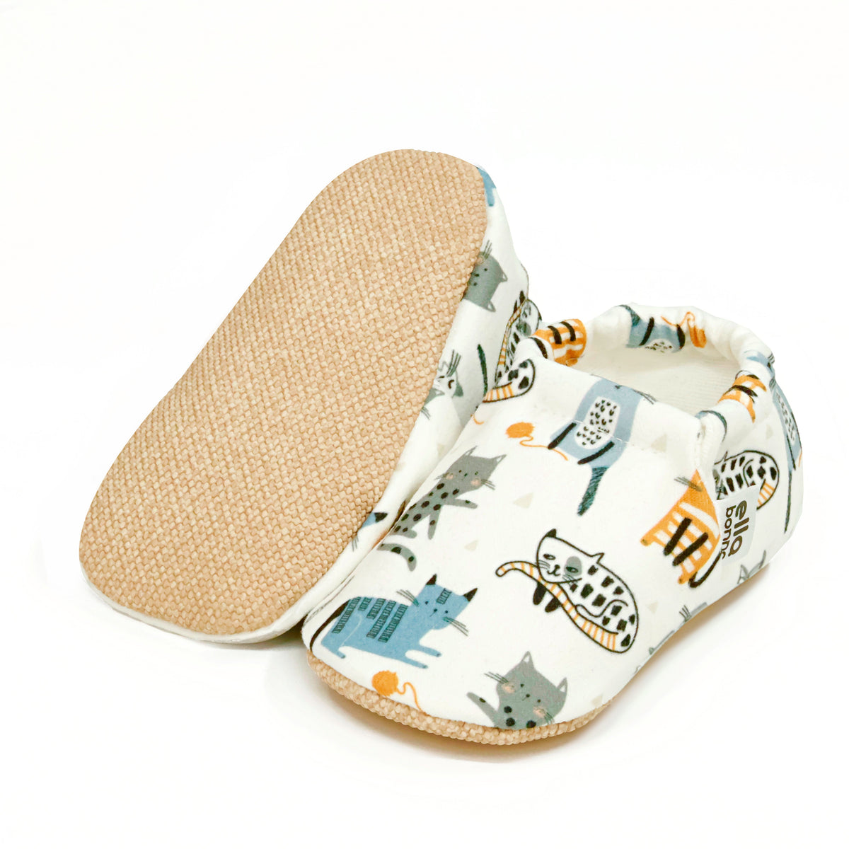 Cream slip-on baby moccasins with illustrated cat print, with one sole facing the camera on a white background.