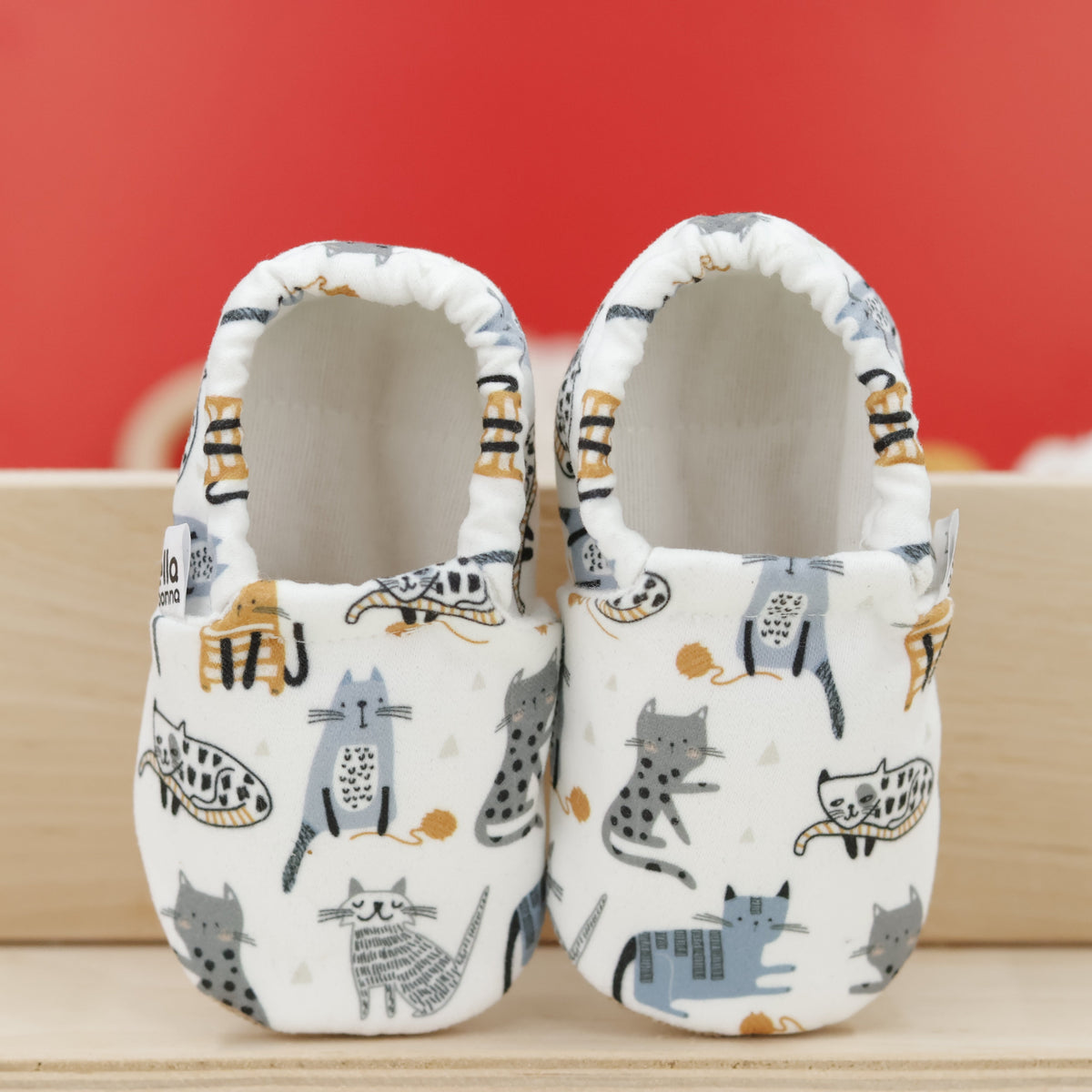 Pair of cream slip-on baby moccasins with illustrated cat print, showing the openings and uppers.