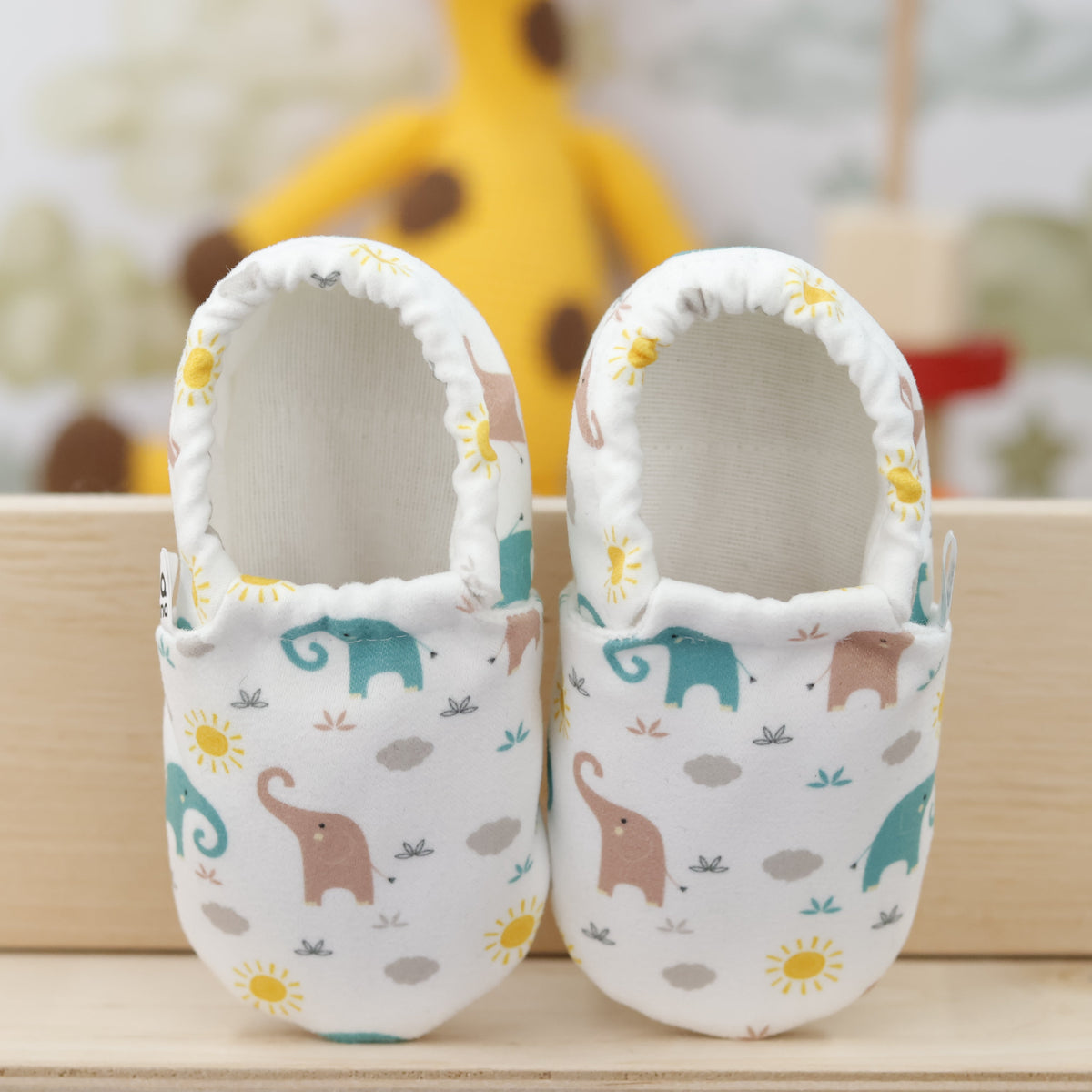 Pair of cream slip-on baby moccasins with pastel elephant print, showing the openings and uppers.