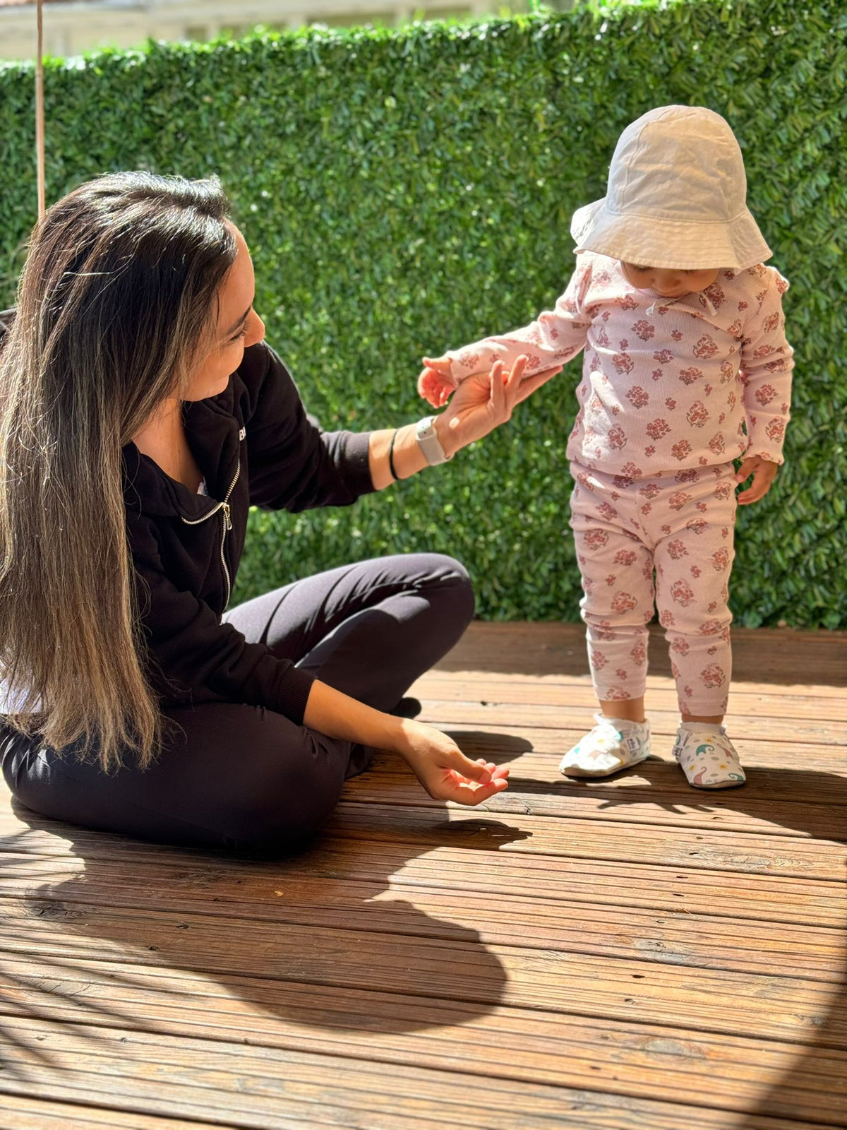 Adult holding a child's hand on a deck while the child wears elephant-print moccasins.