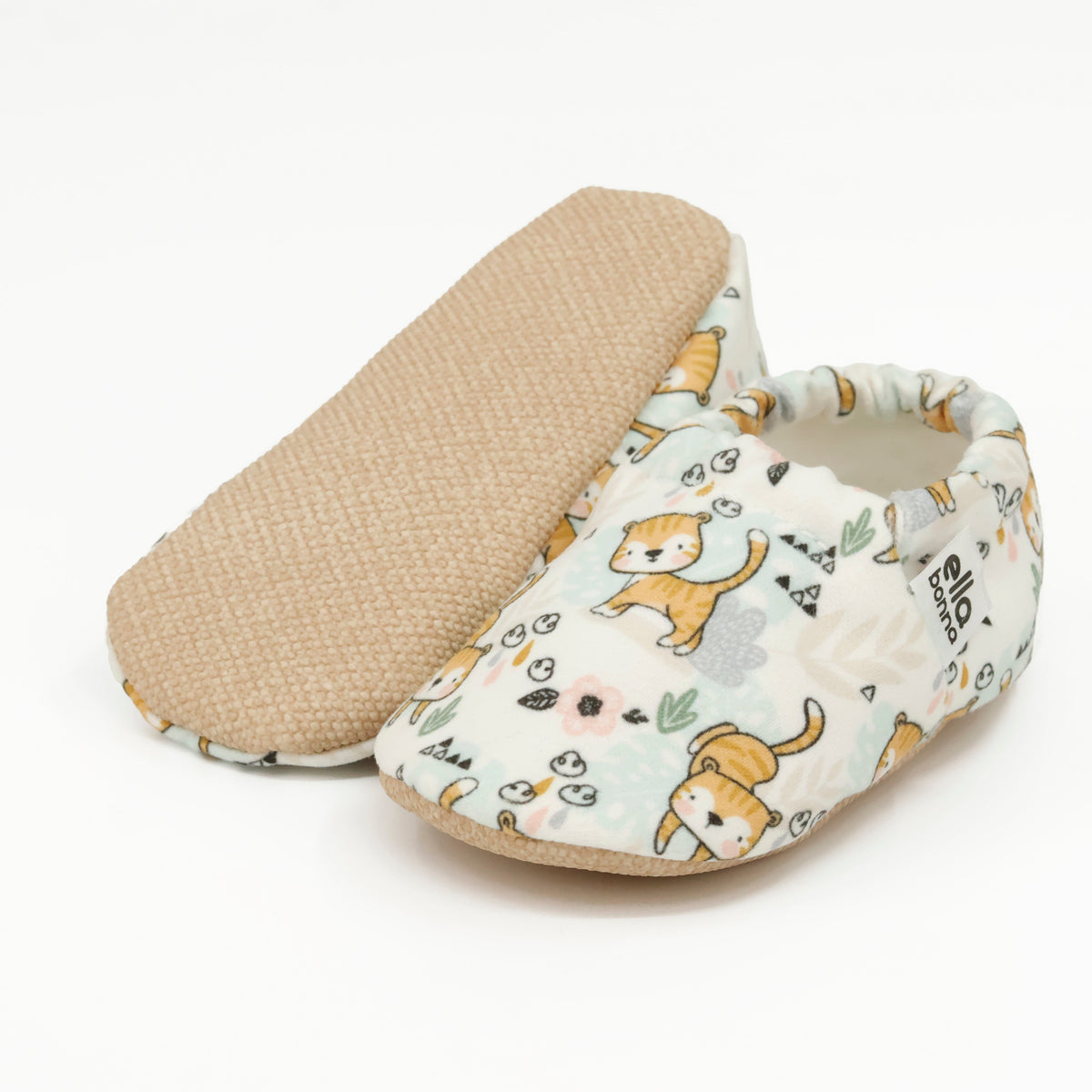 Cream slip-on baby moccasins with small yellow cat print, with one sole facing the camera on a white background.