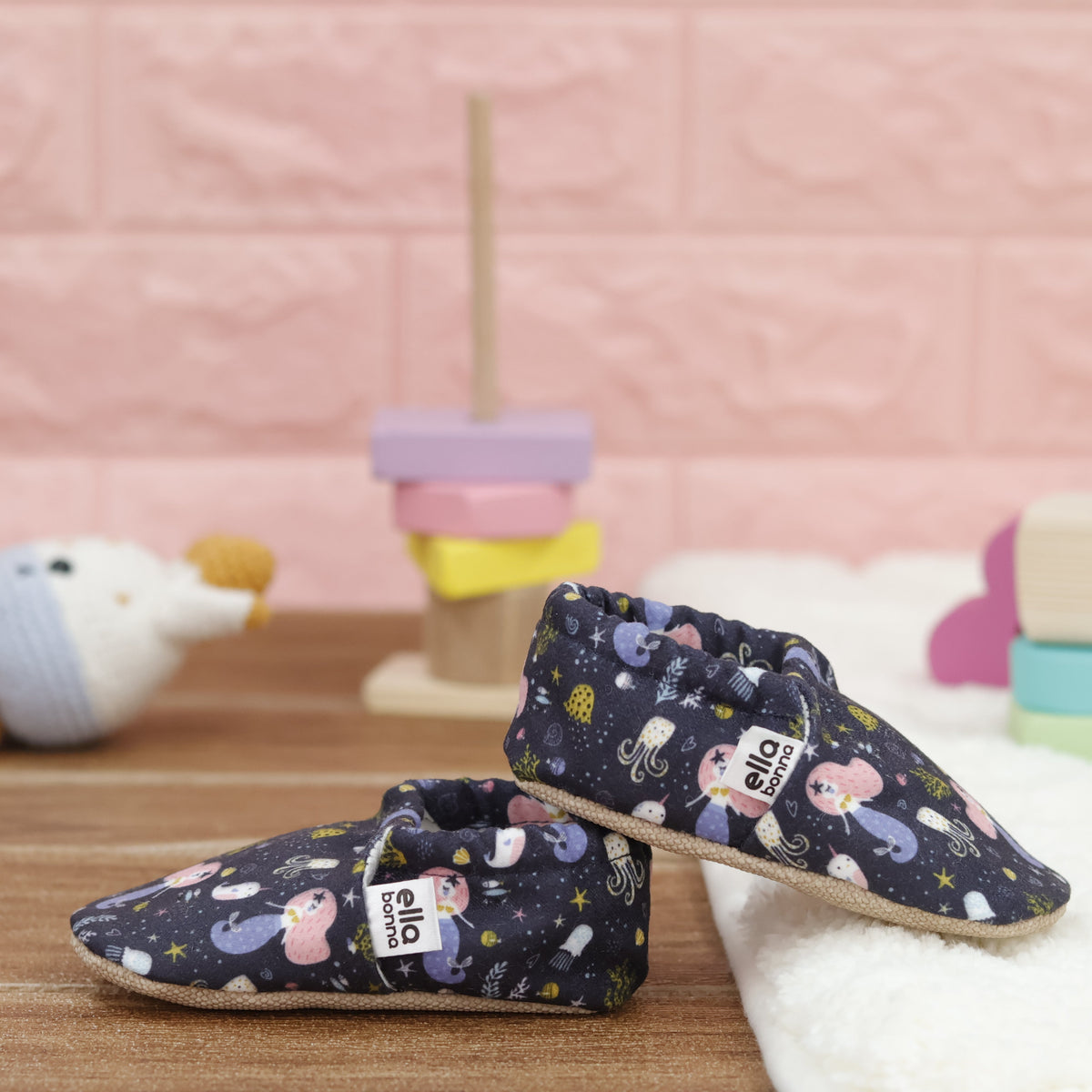 Navy slip-on baby moccasins with mermaids and sea-creature print arranged together to show the sides and uppers.