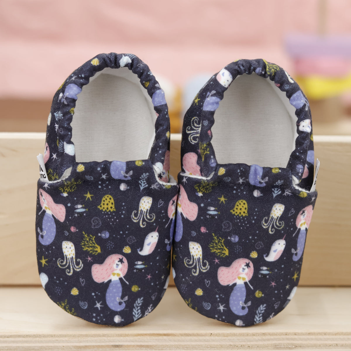Pair of navy slip-on baby moccasins with mermaids and sea-creature print, showing the openings and uppers.